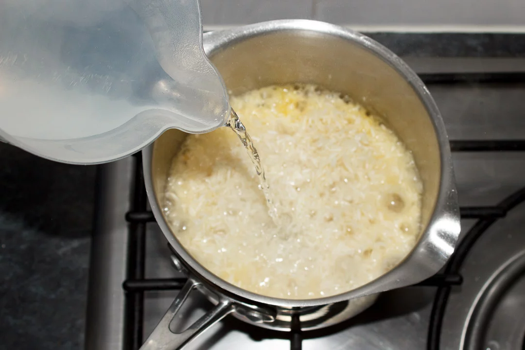 Boiling water being poured over rice in a saucepan