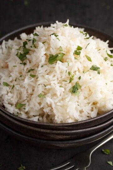 freshly cooked rice scattered with chopped coriander in the top bowl of a stack of 3 with a fork next to it