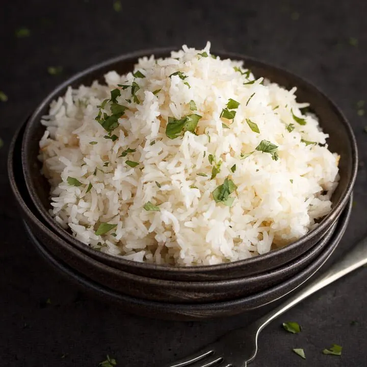 freshly cooked rice scattered with chopped coriander in the top bowl of a stack of 3 with a fork next to it
