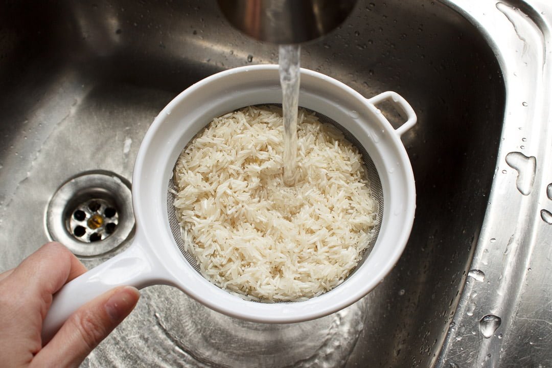 rice being washed in a seive under a tap