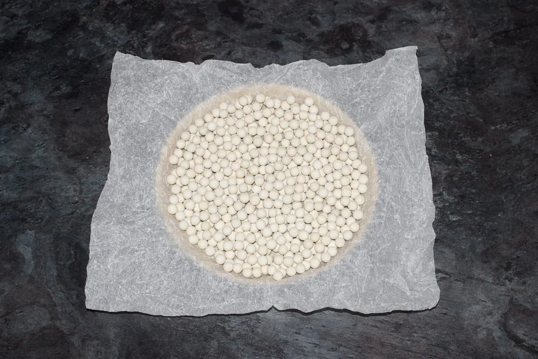 A shortcrust pastry case lined with baking paper and baking beans