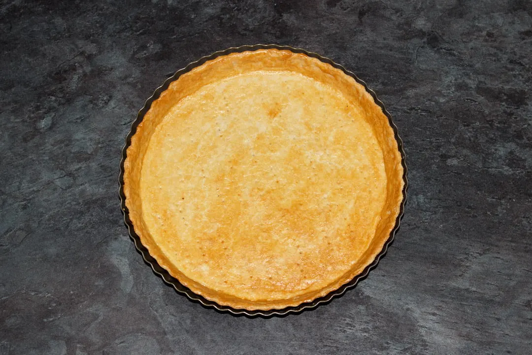Blind baked shortcrust pastry case in a round fluted tart tin on a work surface