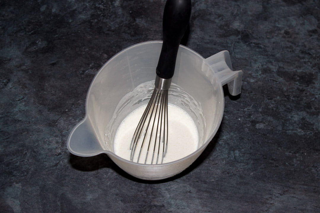Milk and flour whisked to a paste in a plastic jug with a hand whisk