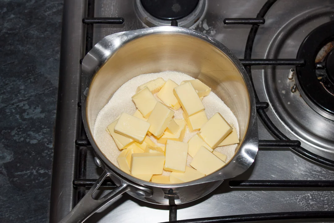 Cubed butter and sugar in a large saucepan set on a stove top
