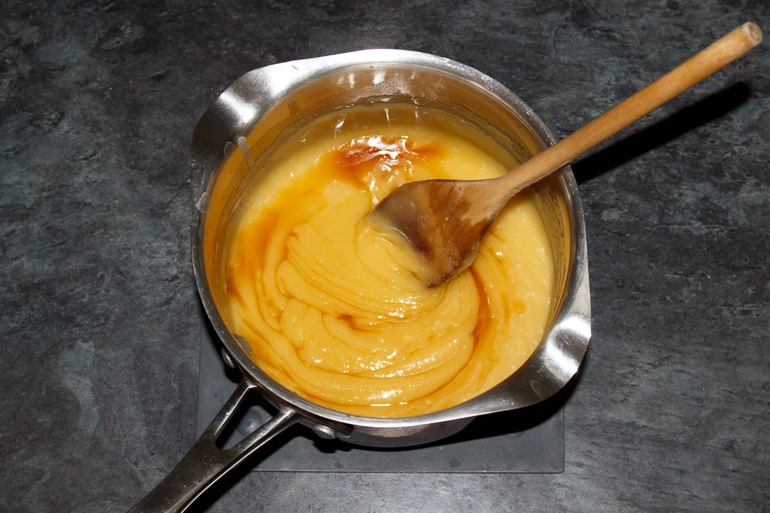 Vanilla, butterscotch essence and salt being mixed into butterscotch tart filling in a large saucepan