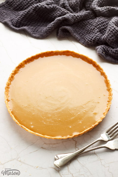 Butterscotch tart on a white marbled worktop with a grey tea towel and 2 forks