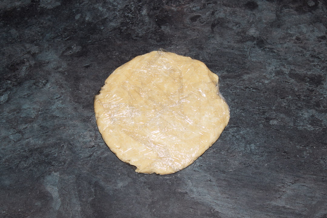 Shortcrust pastry wrapped in clingfilm and flattened into a disc on a worktop