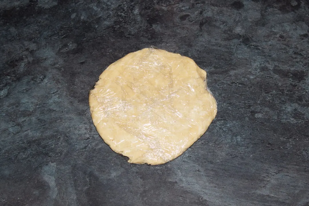 Shortcrust pastry wrapped in clingfilm and flattened into a disc on a worktop