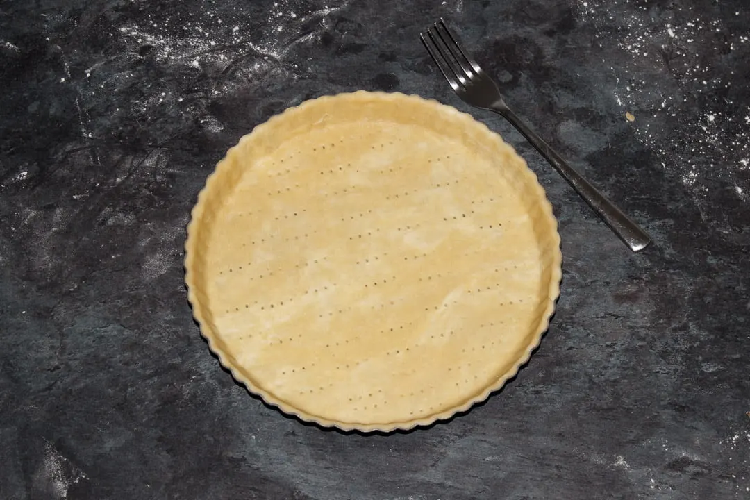 A round fluted tart tin lined with shortcrust pastry and pricked all over with a fork