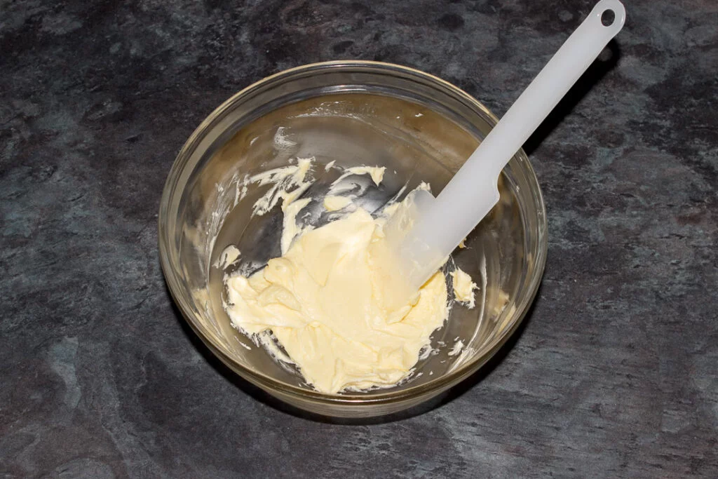 Softened butter in a glass bowl with a spatula.