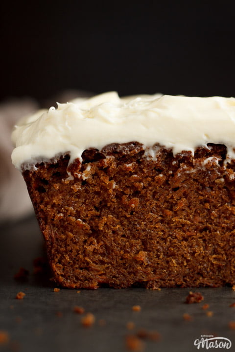 Carrot loaf cake topped with cream cheese frosting on a worktop with a cloth in the background