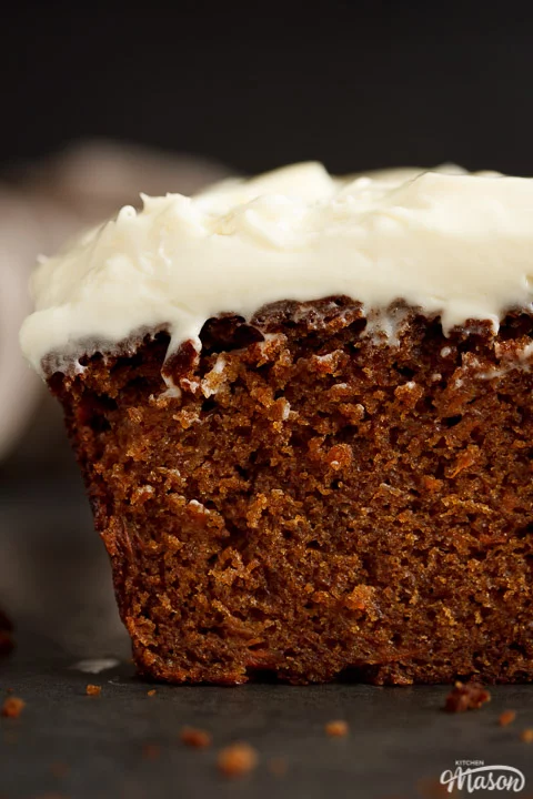 The front of a sliced carrot loaf cake topped with cream cheese frosting. A linen napkin is in the background.