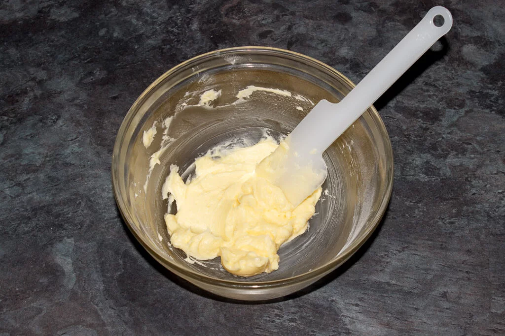 Softened butter and icing sugar beaten together in a glass bowl with a spatula.