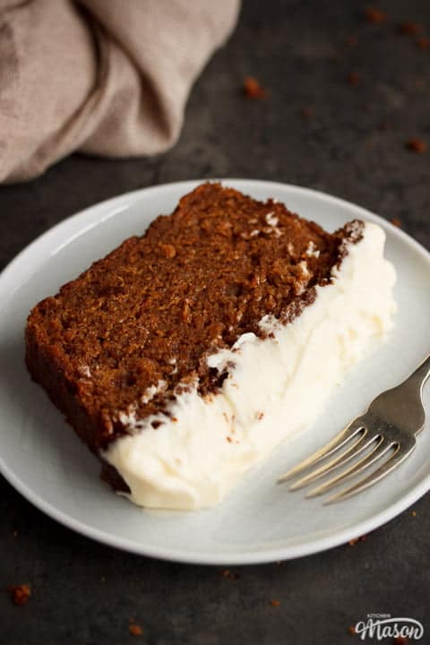 A slice of carrot cake on a pale plate with a fork, with a linen napkin to the side.