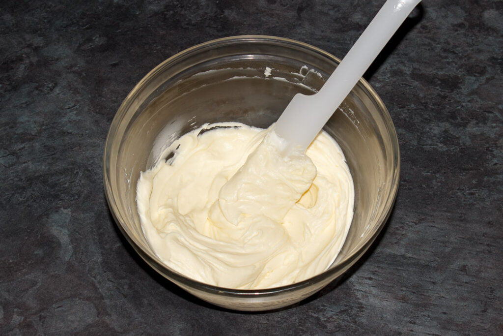 Cream cheese frosting in a glass bowl with a spatula.