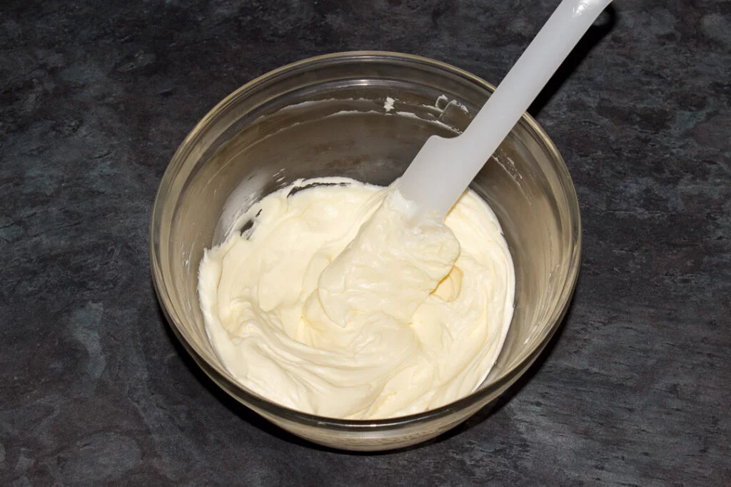 Cream cheese frosting in a glass bowl with a spatula.