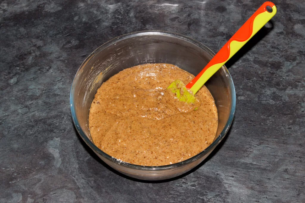 Partially complete carrot loaf cake batter in a glass bowl with a spatula.