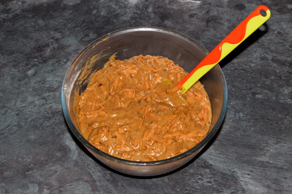 Carrot loaf cake batter in a glass bowl with a spatula.
