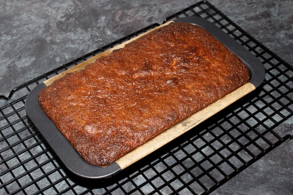 Baked carrot loaf cake in a loaf tin on a cooling rack.