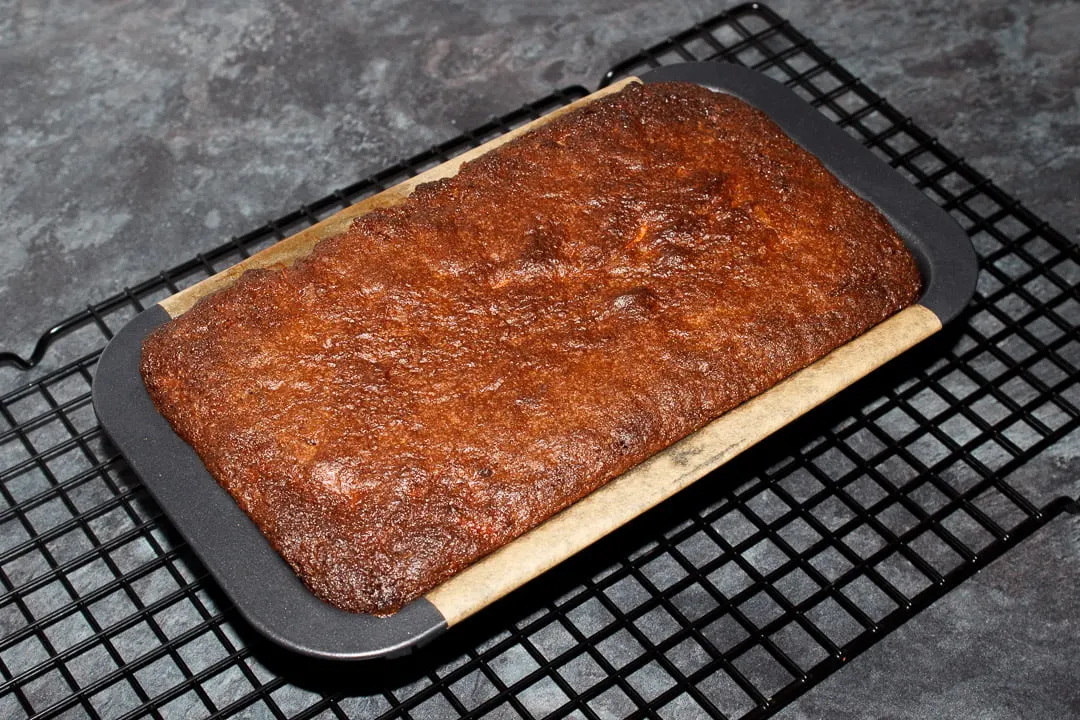 Baked carrot loaf cake in a loaf tin on a cooling rack