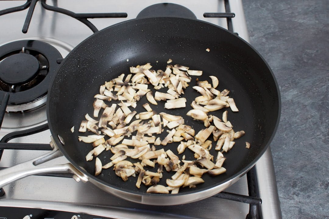 Chopped mushrooms cooking a large frying pan on a hob