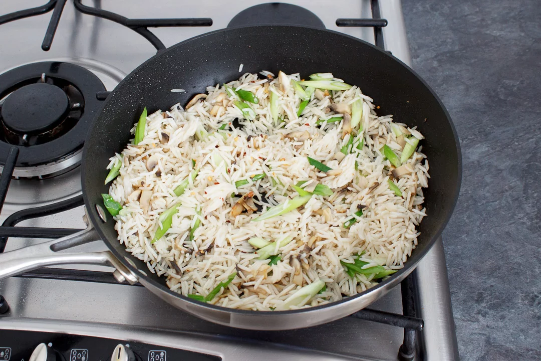 Chopped mushrooms, spring onion and cooked rice frying in a large frying pan on a hob