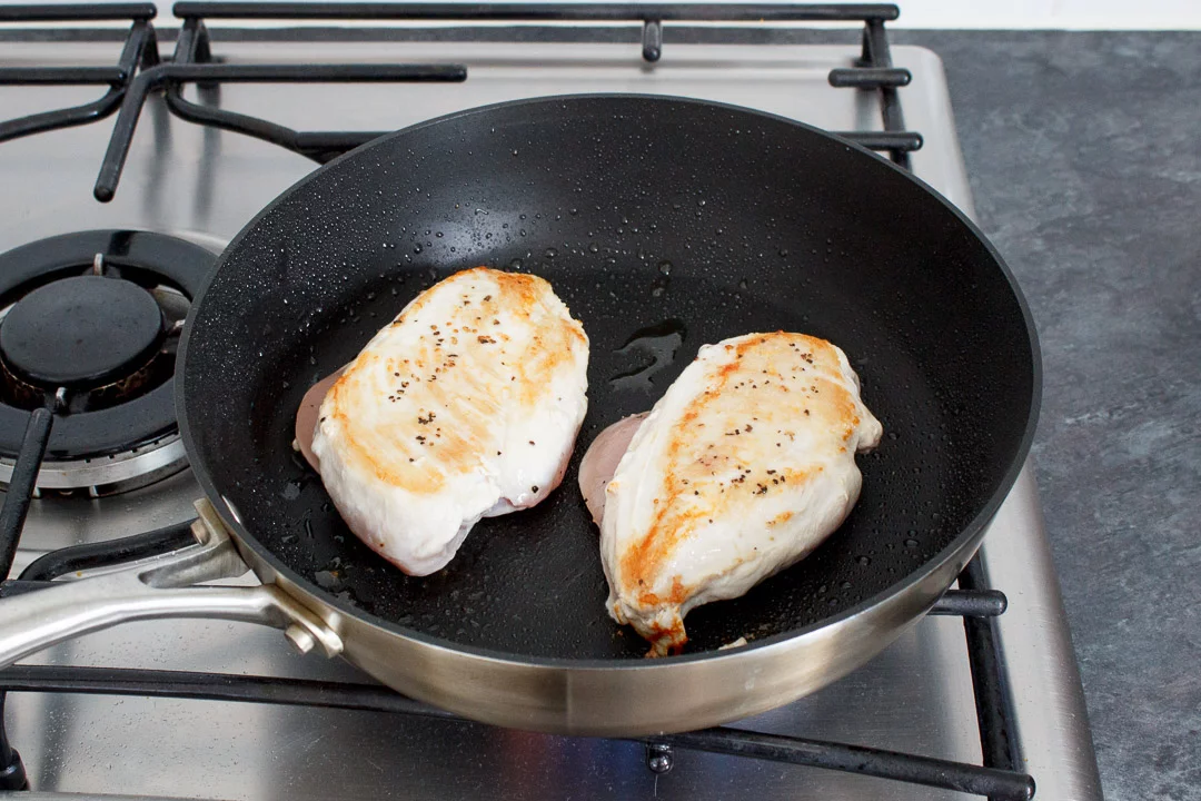 2 chicken breasts frying in a large frying pan on a hob