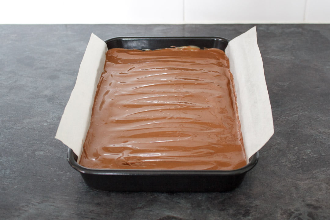 Melted chocolate smoothed on top of the caramel layer in a lined rectangular baking tin.