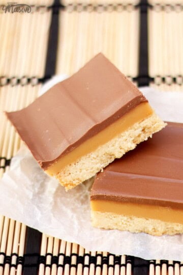 A couple of slices of millionaire's shortbread on baking paper set over bamboo matting.