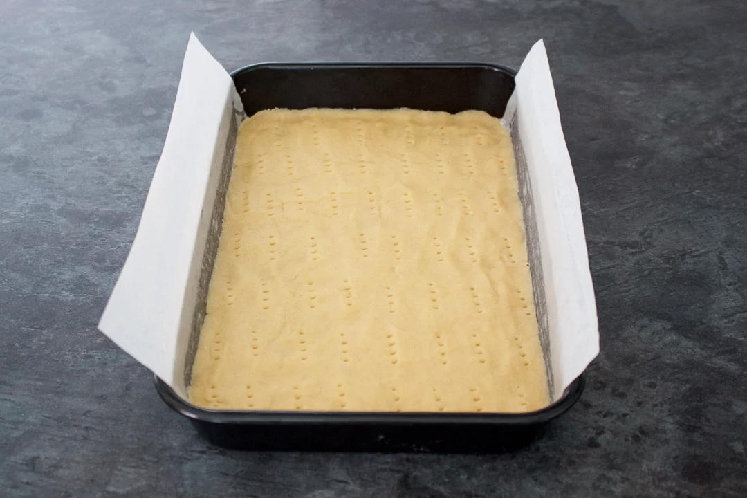 Shortbread dough pressed into the base of a lined rectangular baking tin