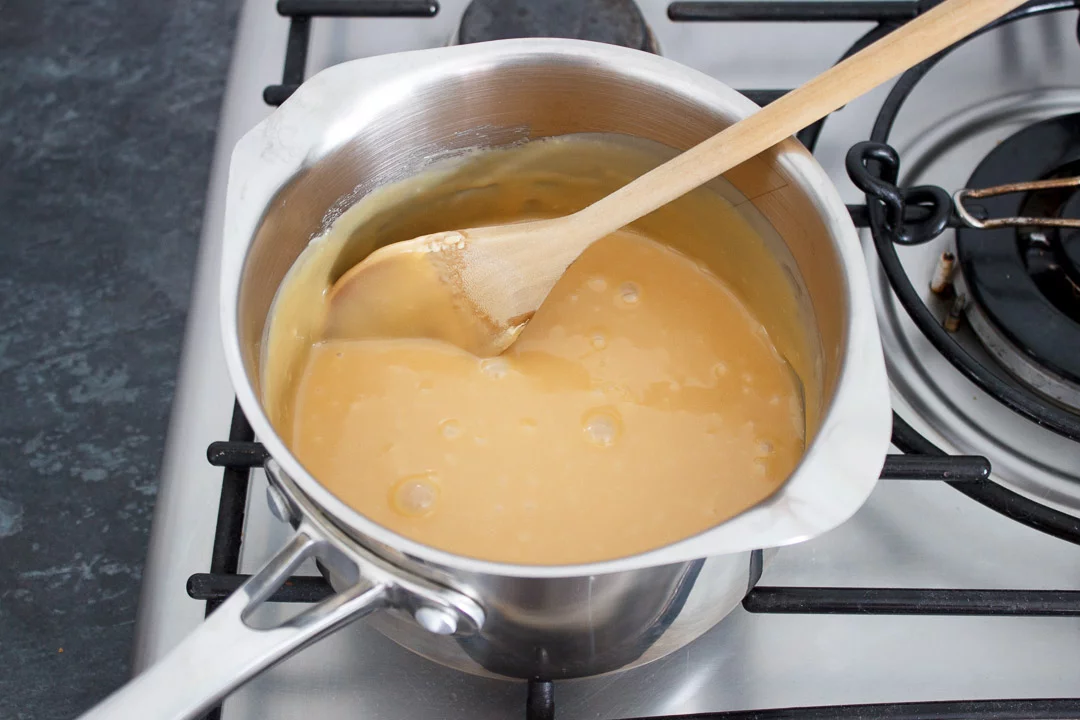Cooked caramel in a large saucepan set over a low heat with a wooden spoon.
