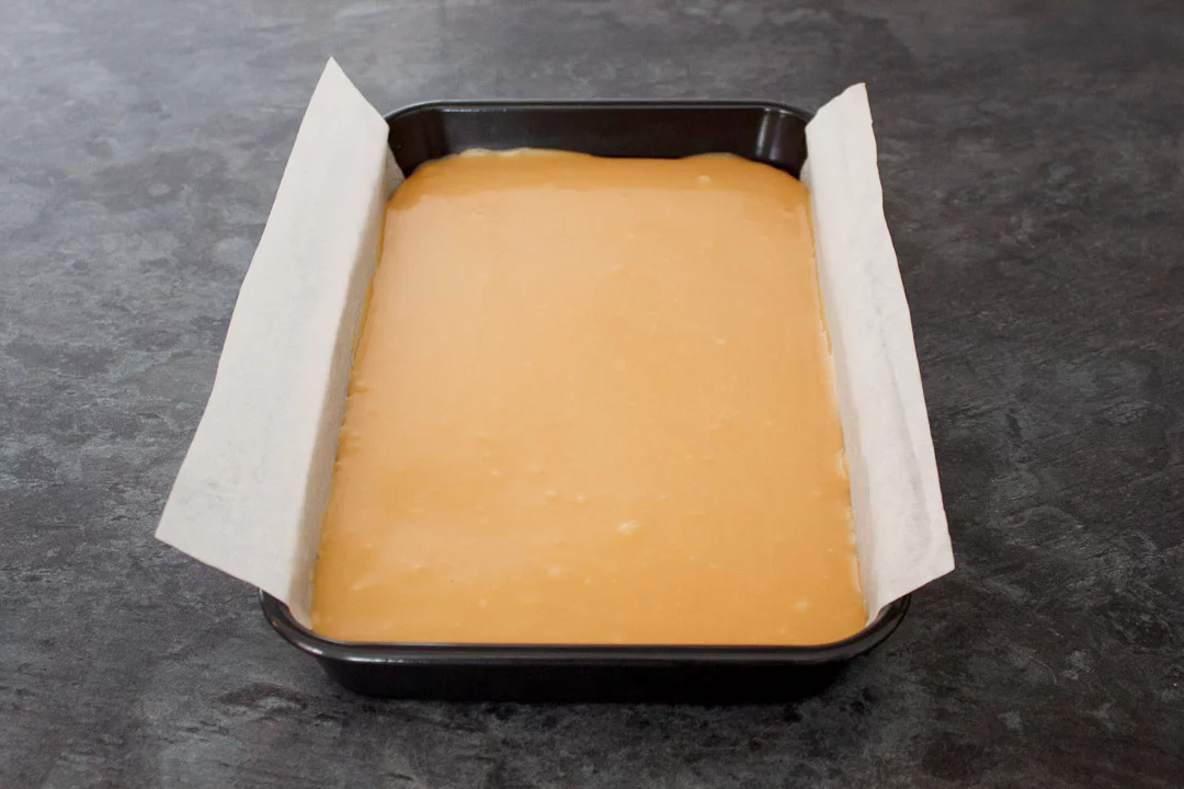 Caramel smoothed over the shortbread biscuit base in a lined rectangular baking tin.