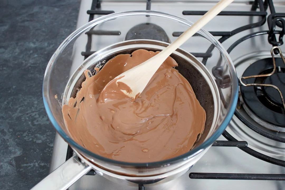 Milk chocolate being melted in a glass bowl set over a pan of barely simmering water on the hob.