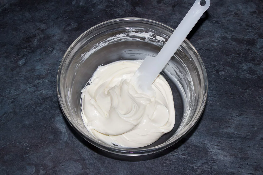 Cream cheese and caster sugar being beaten until smooth in a glass bowl with a spatula
