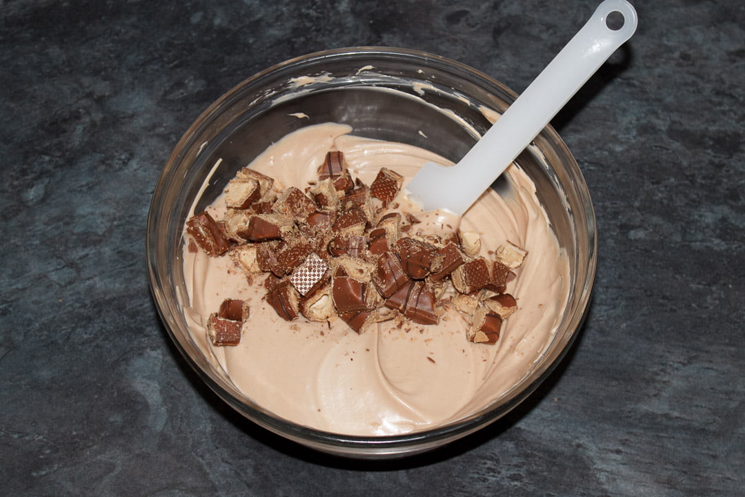 Kinder Bueno cheesecake filling and Kinder Bueno pieces in a glass bowl with a spatula