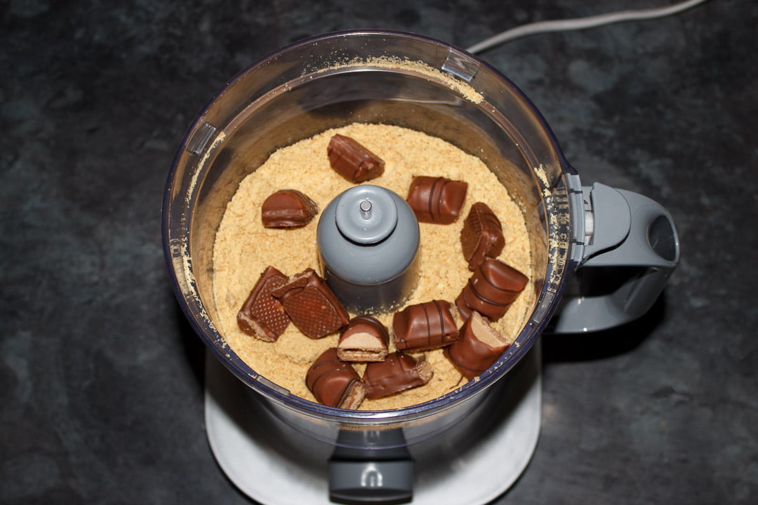 Crushed up digestive biscuits in a food processor with pieces of Kinder Bueno bars