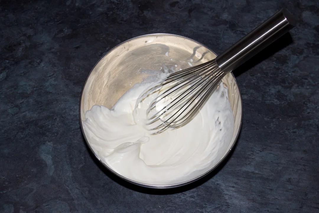 Double cream whipped to soft peaks in a metal bowl with a balloon whisk