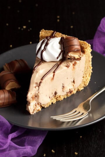 A slice of Kinder Bueno cheesecake on a plate with a fork and Kinder Bueno pieces with purple tulle in the background