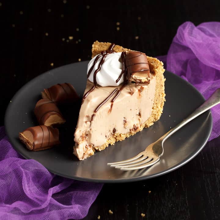 A slice of Kinder Bueno cheesecake on a plate with a fork and Kinder Bueno pieces with purple tulle in the background