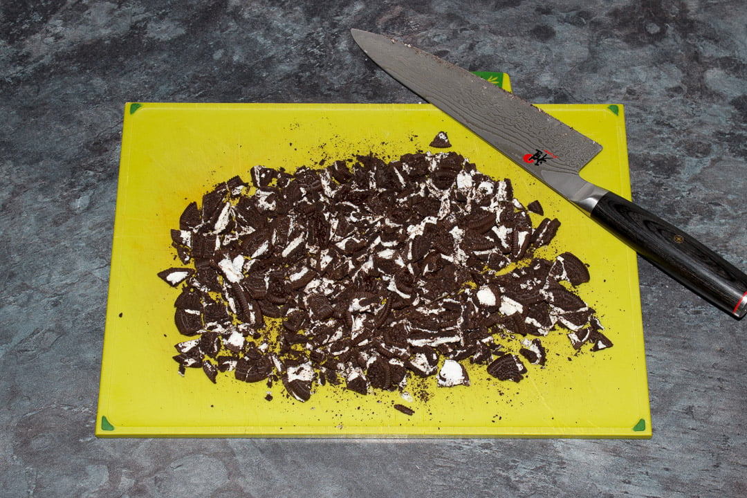 Chopped Oreos on a green chopping board with a large sharp knife
