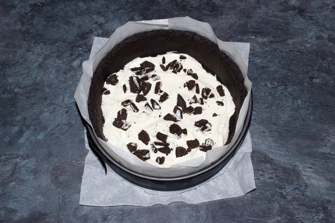 Springform pan lined with an Oreo crumb base and sides, being filled with a cheesecake mixture and chopped Oreos