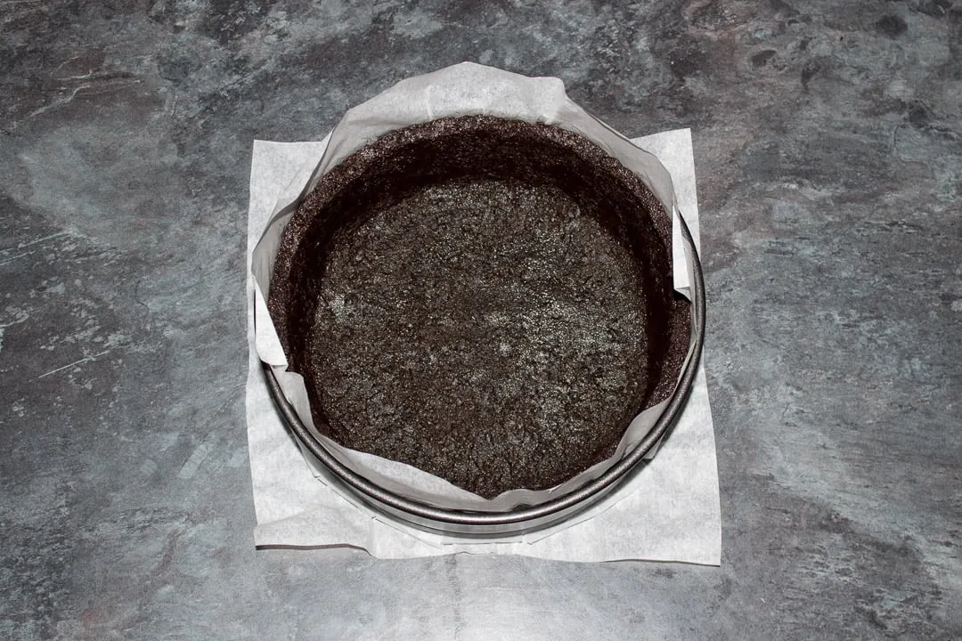 A lined springform pan with buttery Oreo crumbs pressed into the base and sides