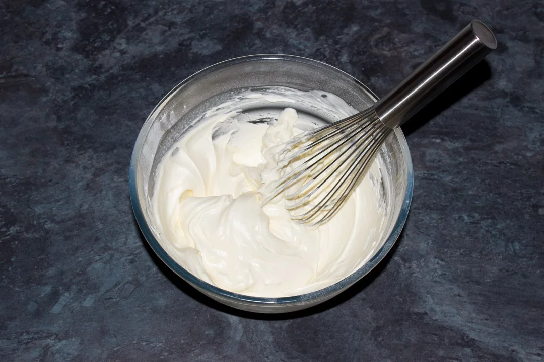 Cream and icing sugar whipped to stiff peaks in a glass bowl with a hand whisk
