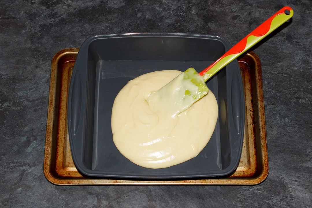 White chocolate fudge being poured into a silicone baking pan and smoothed out with a green spatula