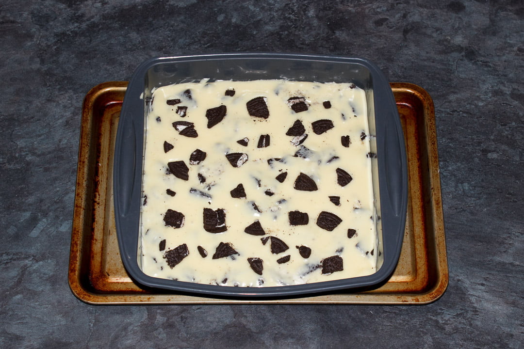 Oreo fudge in a silicone baking pan with roughly chopped Oreos randomly pressed in over the top