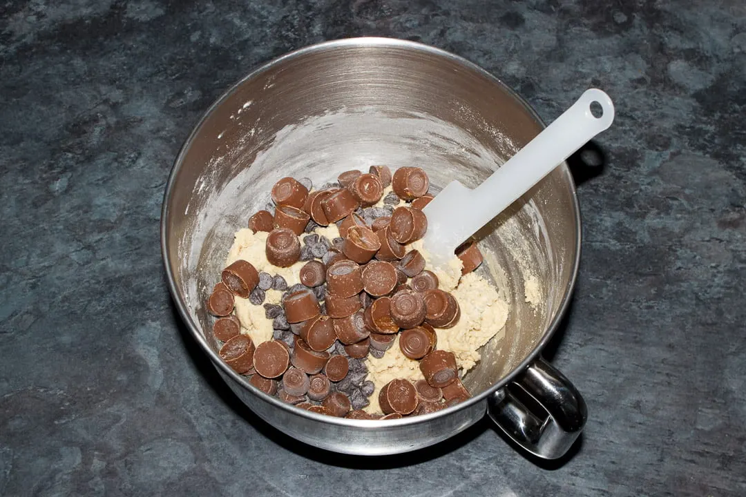 Cookie dough, Rolos and chocolate chips in the bowl of an electric stand mixer with a spatula