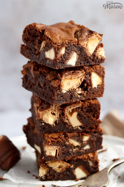 Kinder Bueno Brownies in a stack of 5 on a plate with a fork and 3 pieces of Kinder Bueno. With a light brown napkin and more Kinder Bueno pieces in the background.