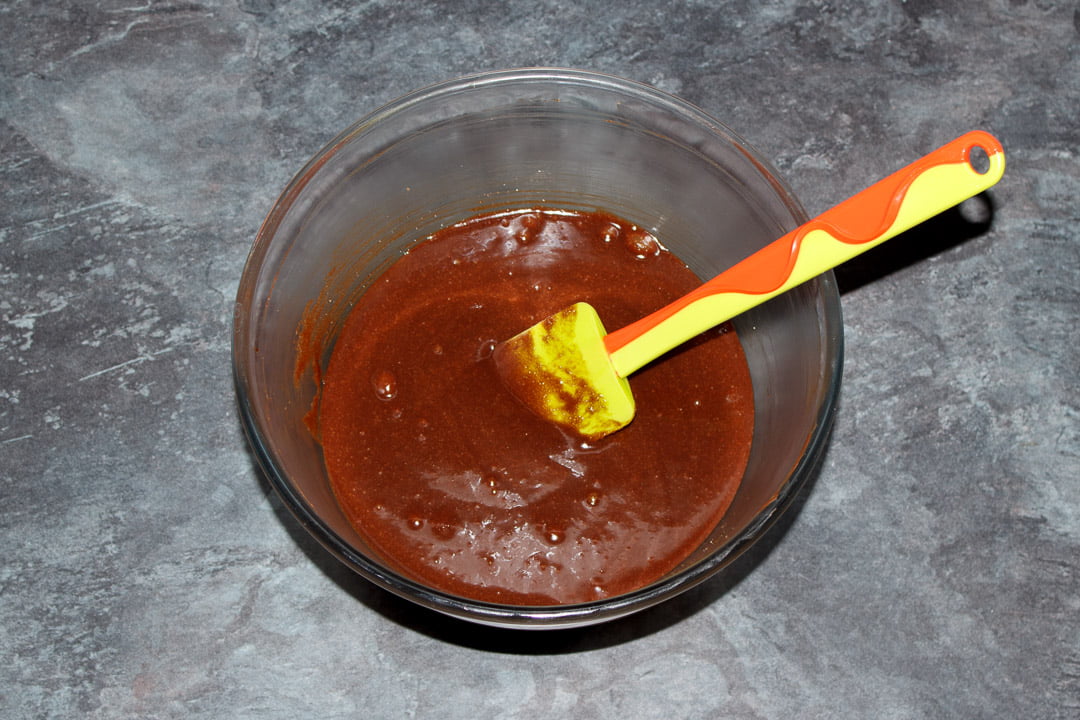 Butter, dark chocolate, eggs and sugar beaten together in a glass bowl with a green spatula