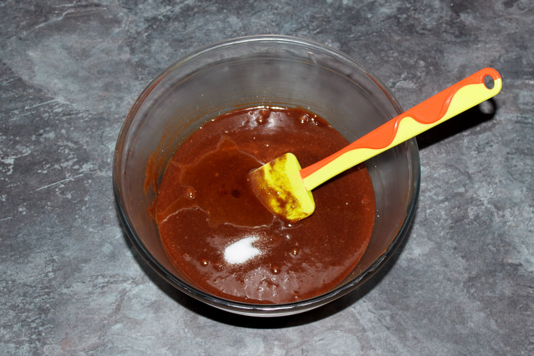 Butter, dark chocolate, eggs, sugar vanilla and salt beaten together in a glass bowl with a green spatula