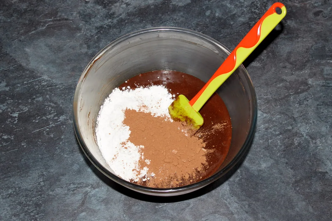 Unmixed brownie batter in a glass bowl with a green spatula